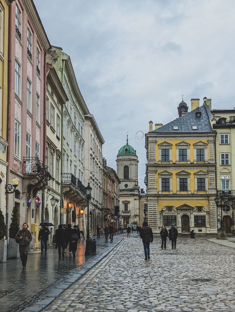 Cobblestone street in Lviv's old town with historical buildings and pedestrians on a rainy day.
